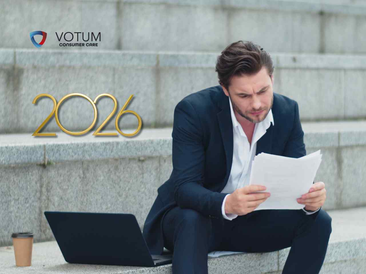 Mężczyzna w garniturze siedzi na schodach obok laptopa i z przejęciem analizuje trzymane w rękach dokumenty, a obok niego widnieje złoty napis 2026.