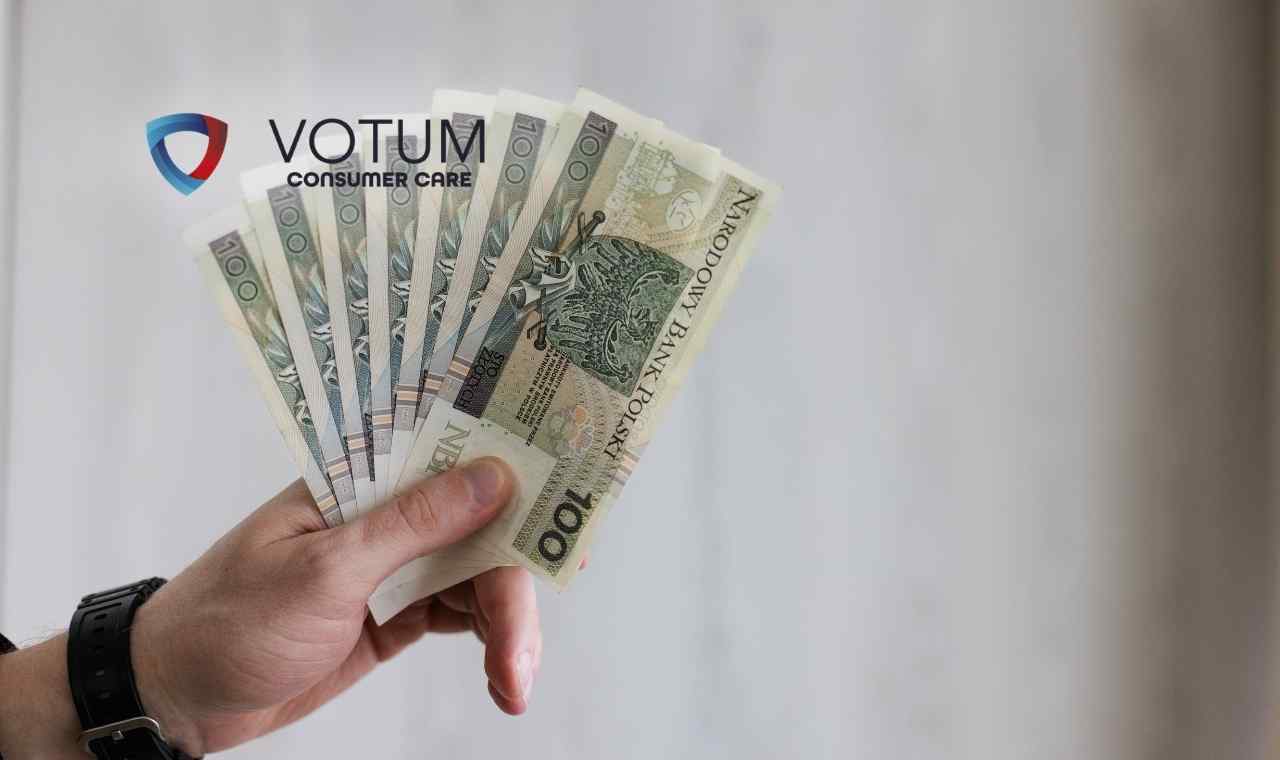 Dłoń trzyma rozłożone w wachlarz banknoty o nominale stu złotych na jasnym, jednolitym tle.