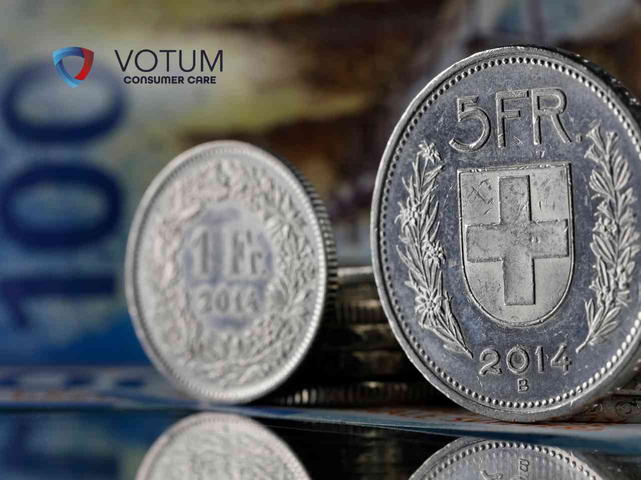 Srebrne monety o nominałach 5 i 1 frank szwajcarski na tle banknotu stufrankowego