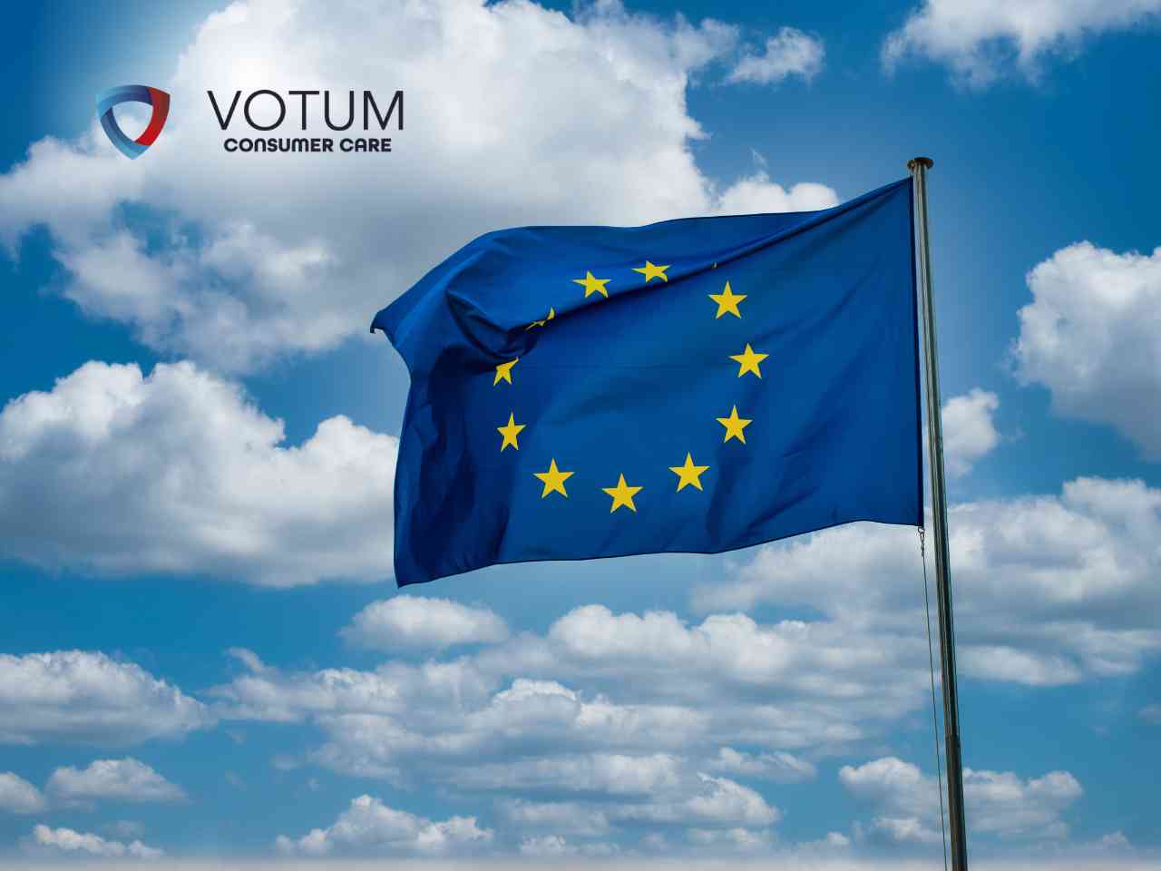 Niebieska flaga Unii Europejskiej z żółtymi gwiazdami powiewająca na masztu na tle błękitnego nieba z białymi chmurami.