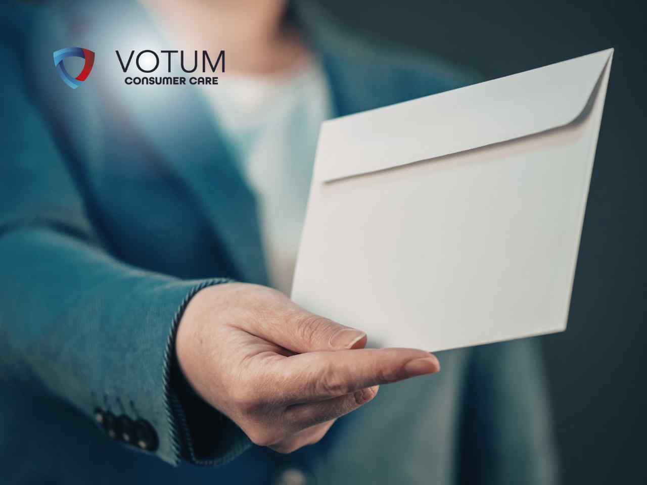 Zbliżenie na dłoń osoby w eleganckiej marynarce, która podaje białą, zamkniętą kopertę.