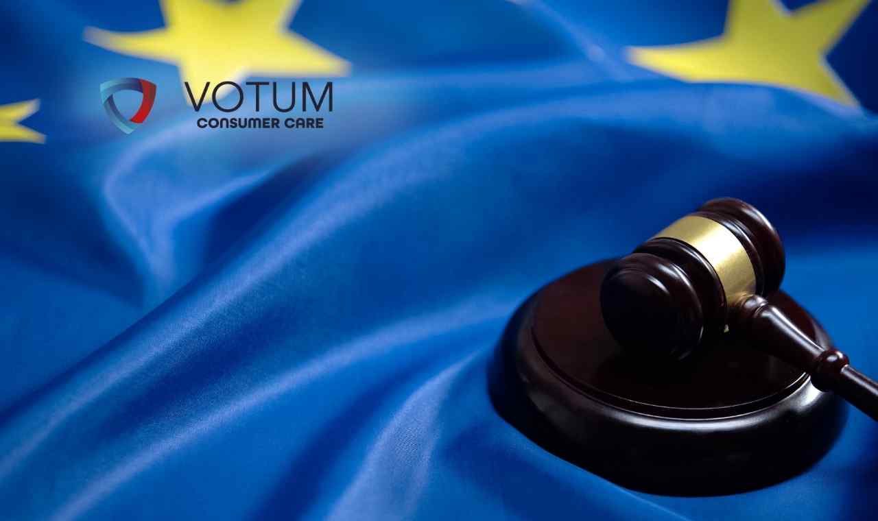 Drewniany młotek sędziowski spoczywający na podstawce, ułożony na pofalowanej fladze Unii Europejskiej z charakterystycznymi żółtymi gwiazdami na niebieskim tle.
