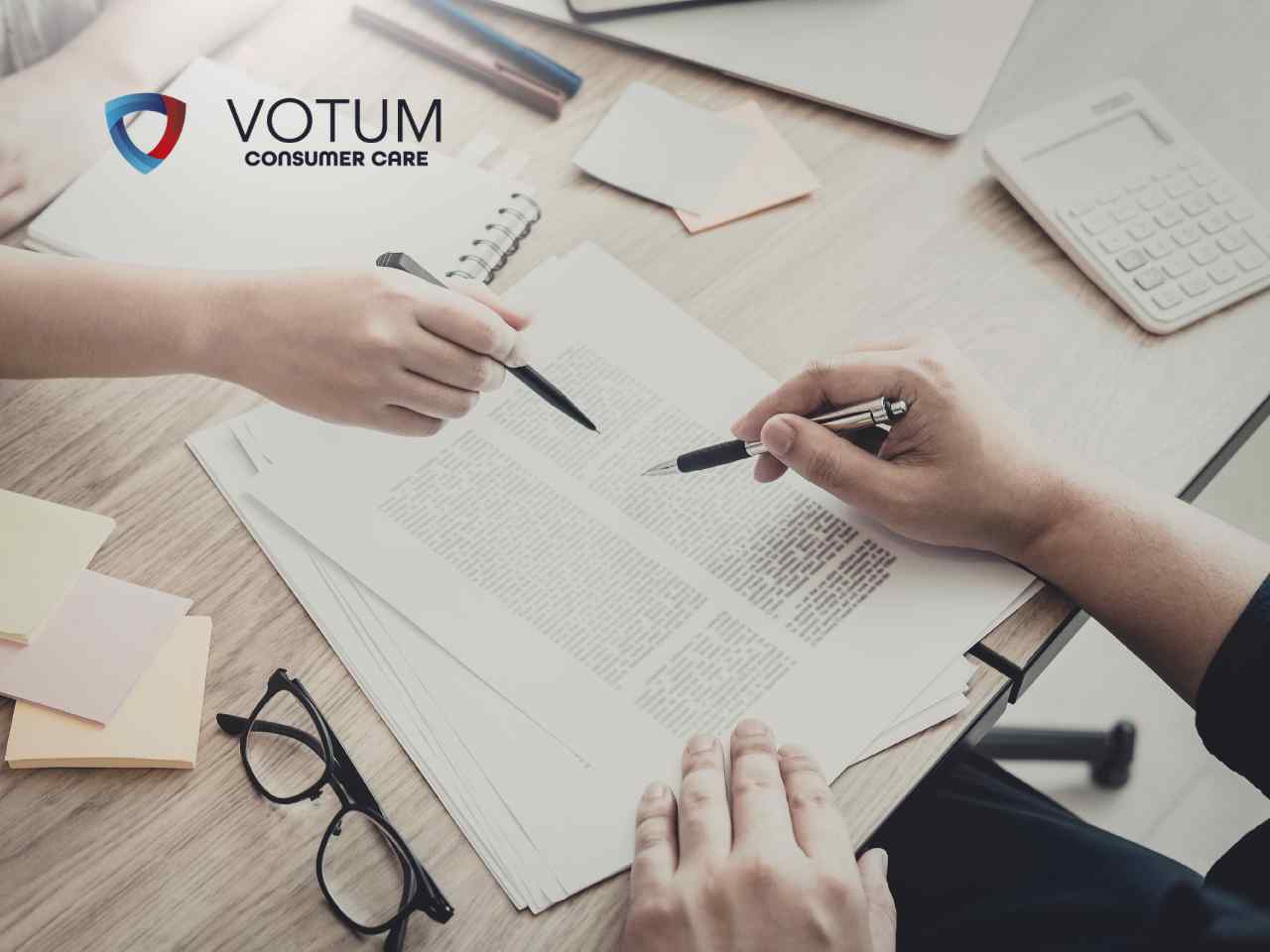Zbliżenie na dłonie dwóch osób analizujących dokumenty przy biurku, wskazujących długopisami konkretne zapisy w umowie. W lewym górnym rogu znajduje się logotyp Votum Consumer Care, a na stole widoczny jest kalkulator i okulary.