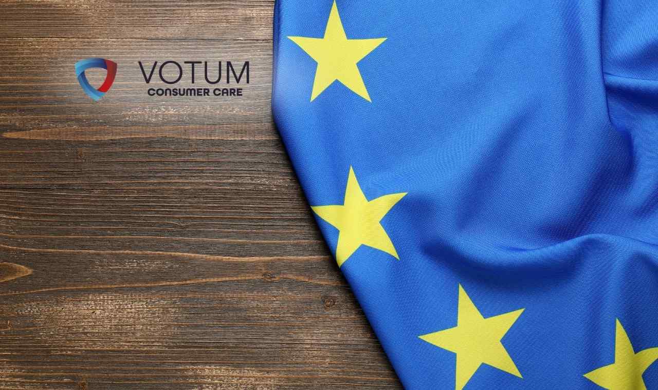 Fragment flagi Unii Europejskiej z żółtymi gwiazdami na niebieskim tle, ułożonej na ciemnym, drewnianym blacie o wyraźnej strukturze słojów.