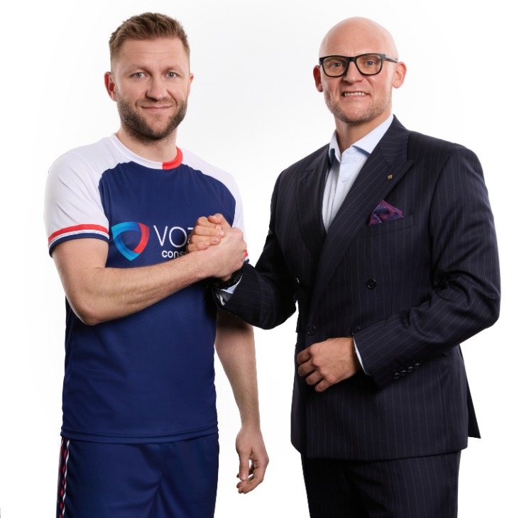Jakub-Blaszczykowski-Pawel-Wojcik-pomoc-frankowiczom Jakub Błaszczykowski w sportowym stroju marki Votum oraz Paweł Wójcik w eleganckim, prążkowanym garniturze wymieniają mocny uścisk dłoni na białym tle.