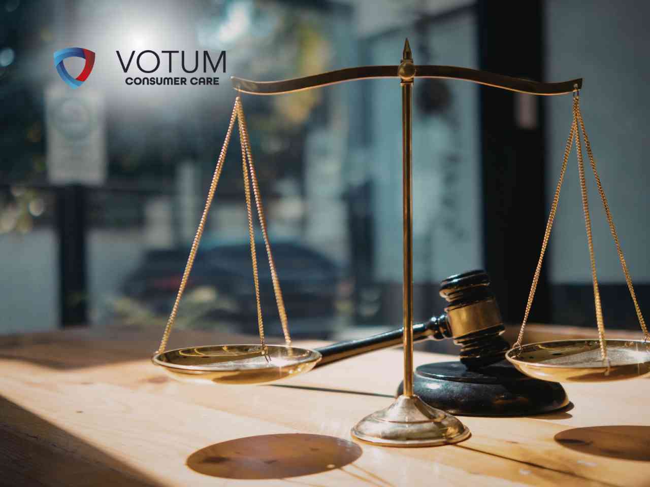 Golden balance scales and a gavel sit on a wooden desk, with the VOTUM Consumer Care logo in the top-left corner, symbolizing justice and legal services.