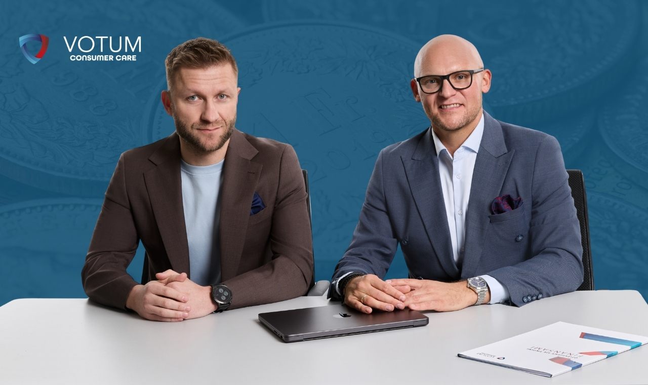 Jakub Błaszczykowski w brązowej marynarce oraz Paweł Wójcik w niebieskim garniturze siedzą obok siebie przy białym biurku, na którym leży zamknięty laptop oraz teczka dokumentów. Tłem jest ciemnoniebieska grafika z motywem monet. W lewym górnym rogu znajduje się logotyp Votum Consumer Care.