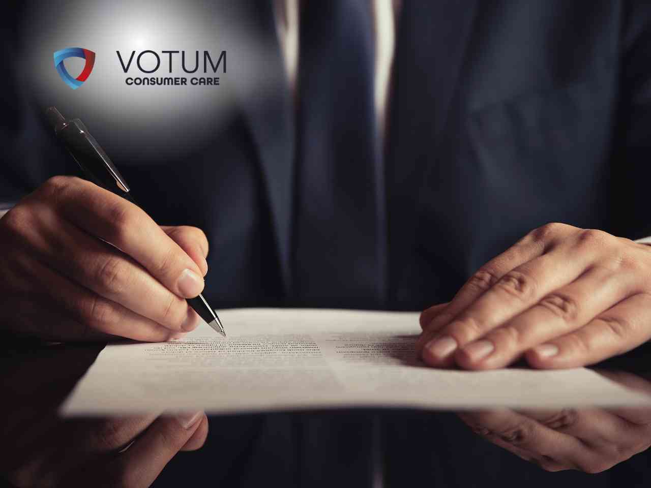 Prawnik w garniturze prezentuje dokument do podpisu klientom siedzącym przy biurku, na którym znajdują się waga szalkowa i młotek sędziowski. W lewym górnym rogu widnieje logotyp Votum Consumer Care.