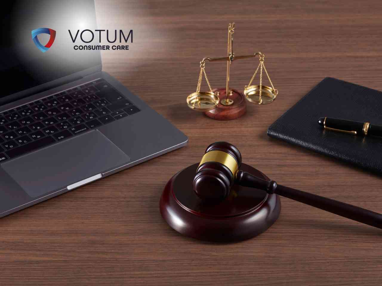 Laptop, scales of justice, wooden gavel, and a black notebook with a gold‑and‑black pen on a wooden desk, with the VOTUM Consumer Care logo in the corner.