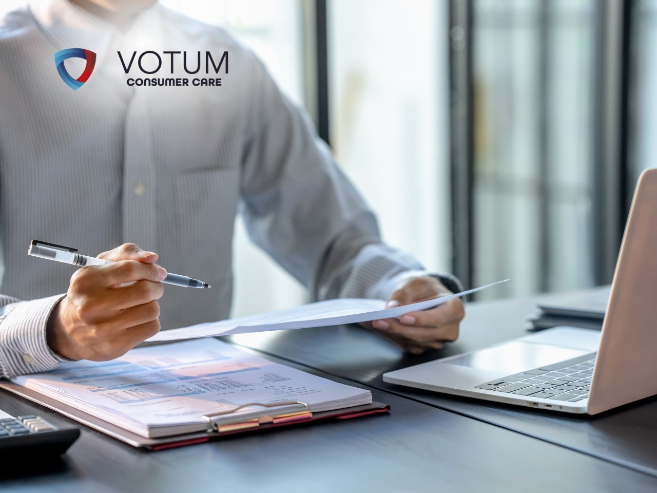 Businessperson reviews documents at a desk with a laptop, VOTUM Consumer Care logo visible in the corner.