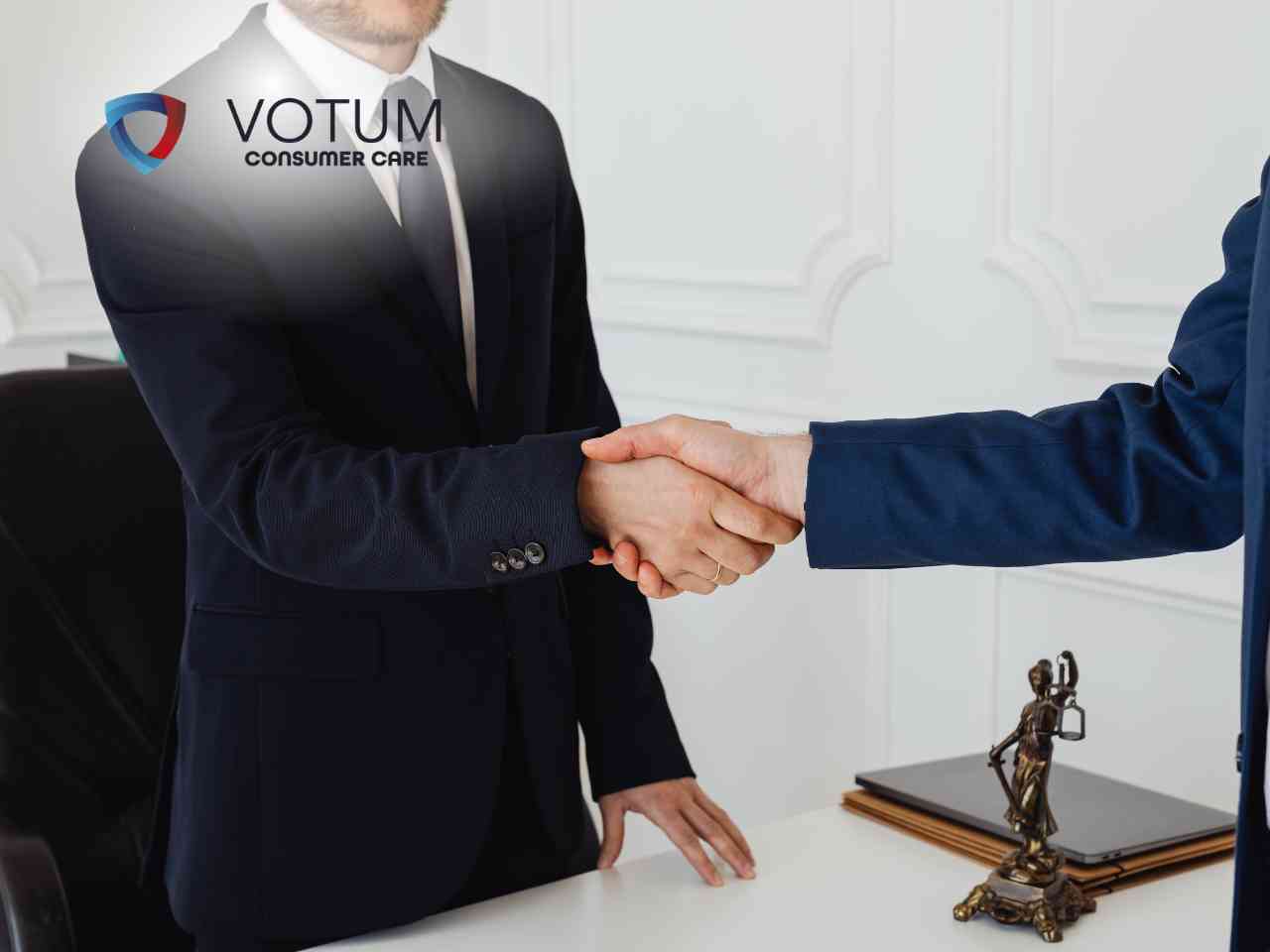 Prawnik w okularach rozmawia przy biurku z parą klientów, tłumacząc zawiłości prawne. Na stole widoczna jest statuetka Temidy oraz otwarte księgi prawnicze. W lewym górnym rogu znajduje się logotyp Votum Consumer Care.
