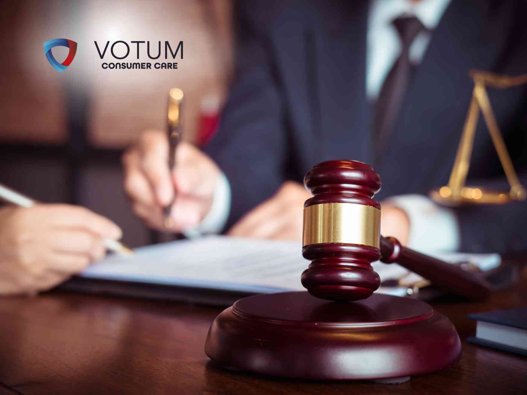 Gavel on a courthouse desk with blurred lawyers signing papers in the background and scales of justice; logo 'VOTUM CONSUMER CARE' visible in the upper left.