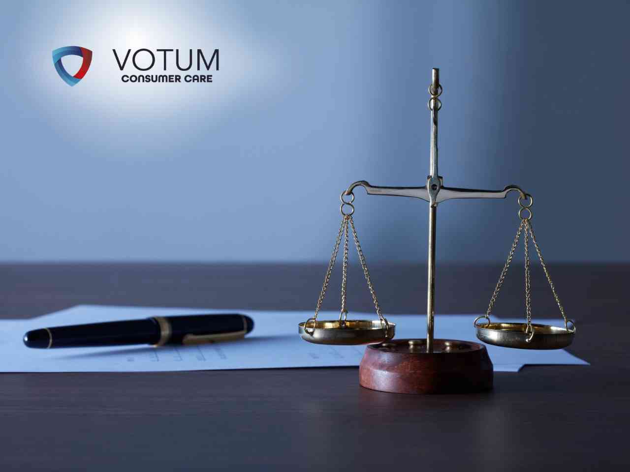 5-sygnalow-sankcja-kredytu-darmowego Scales of justice on a wooden desk with a blue sheet of paper and a pen, logo 'VOTUM Consumer Care' in the top-left corner