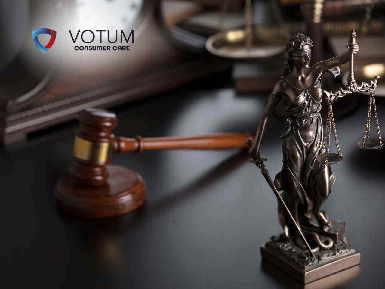 Scena w biurze lub kancelarii; po lewej stronie mężczyzna w ciemnym garniturze i okularach przekazuje dokument kobiecie w beżowej marynarce. W tle widoczny jest drugi mężczyzna, który z niedowierzaniem trzyma się za głowę. Na stole leżą teczki z aktami oraz gazeta.