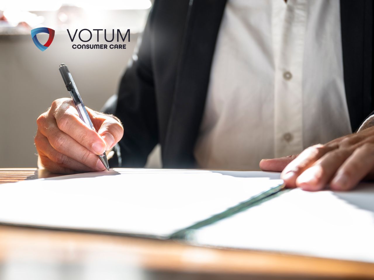 Close-up of a hand signing documents at a desk, with VOTUM Consumer Care logo in the background.