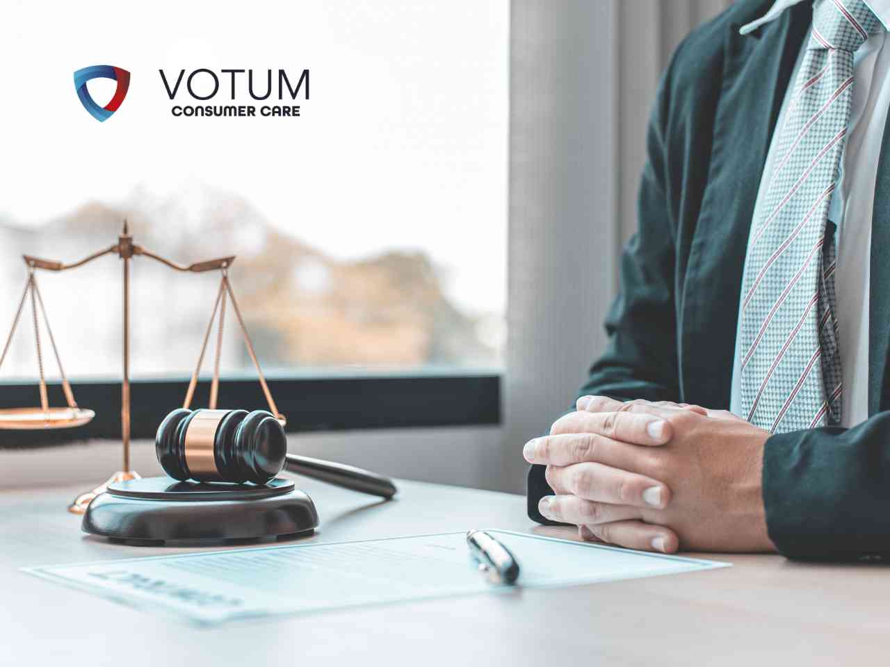 odsetki-od-skredytowanych-kosztow VOTUM Consumer Care logo with scales of justice and gavel on a desk, a suited person’s folded hands visible on the right.