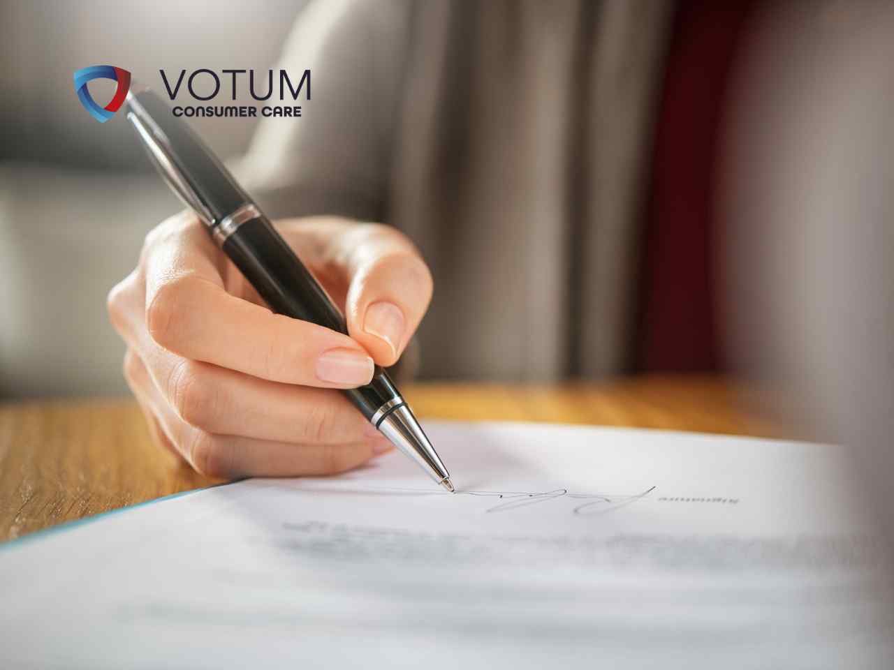 jak-napisac-oswiadczenie-do-banku-skd Close-up of a hand signing a document with a black pen; VOTUM CONSUMER CARE logo appears in the top-left corner.