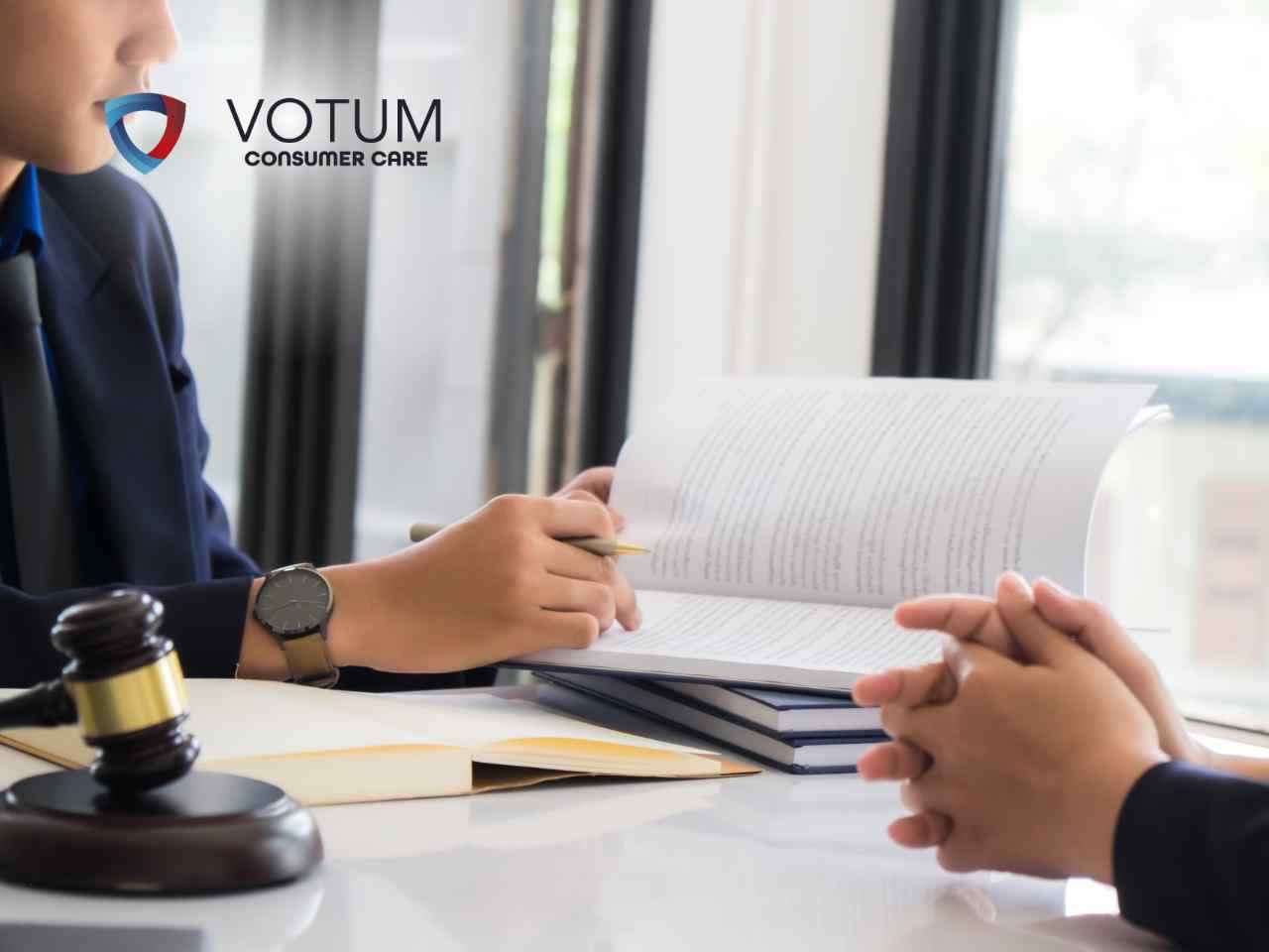 splacony-kredyt-gotowkowy-sankcja-kredytu-darmowego Person signs documents at a desk with a gavel and stacked books; VOTUM Consumer Care logo appears in the top-left corner.