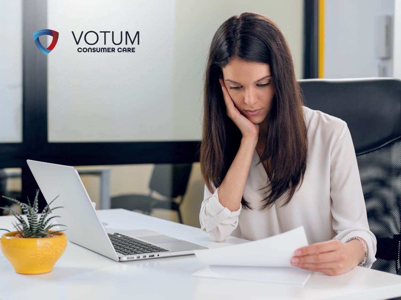 konsultacja-prawna-sankcja-kredytu-darmowego Professional woman at a desk resting her head on her hand while reading a document; VOTUM Consumer Care logo visible on the glass wall behind her.