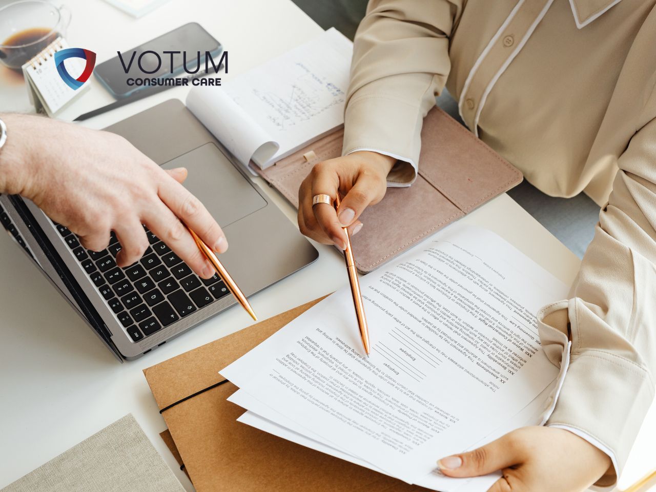 kredyt-konsumencki-dokumenty-umowa Two professionals review printed contracts at a desk, with a laptop and a VOTUM Consumer Care logo.