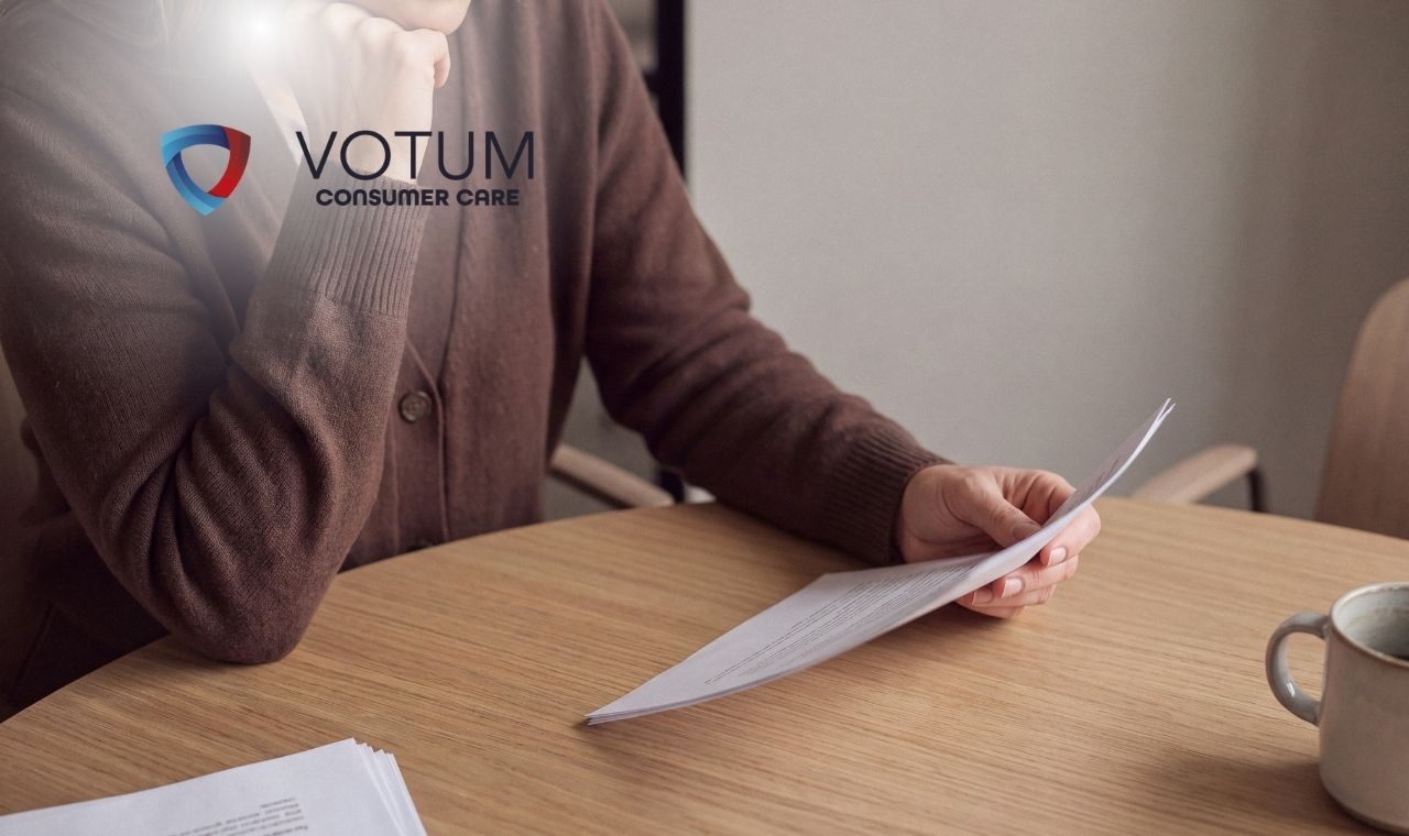 Person signing a document at a desk with a silver laptop nearby and the VOTUM Consumer Care logo visible on the left.